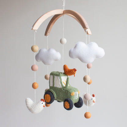 Hand-knitted green tractor and chickens baby mobile with white clouds on a wooden arch.