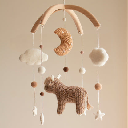 Macro view of a golden-tan crochet moon with white embroidered stars on a baby mobile. Smooth untreated solid alder wood cross-arch hanger for a minimalist artisan nursery mobile.
