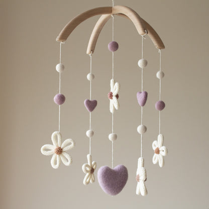Hand-knitted daisy with a beige center and white wool petals. Soft wool hearts and felted balls in purple and ivory on a floral nursery mobile.