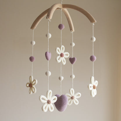 Hand-knitted daisy baby mobile in purple and cream hanging in a modern white nursery.