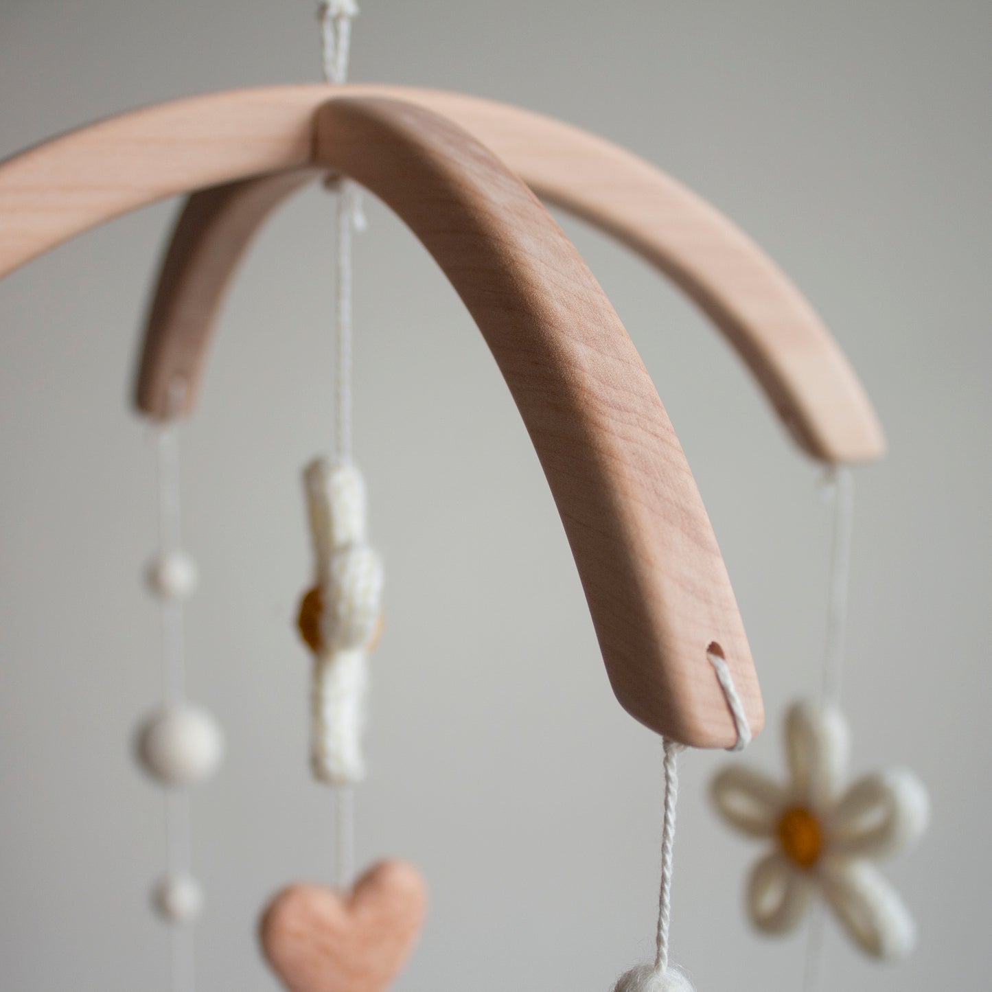 Macro detail of a sustainable wooden arch and ivory wool clouds on a handmade baby mobile. This image emphasizes the high-quality, natural materials and safety standards that define our artisan brand. Handcrafted in the UK, our mobiles use only non-toxic, eco-friendly components to create a safe sensory experience. This focus on material transparency builds trust with affluent buyers who prioritize ethical sourcing and vetted quality.