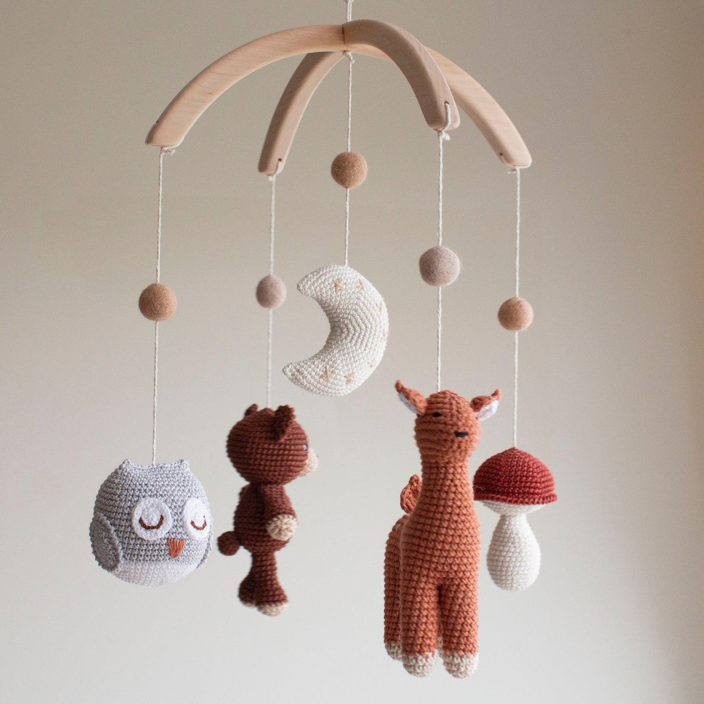 Close-up of a sleepy gray and white crochet owl with intricate stitch work. Minimalist forest animal nursery mobile hanging above a white crib in a nature-inspired baby room.