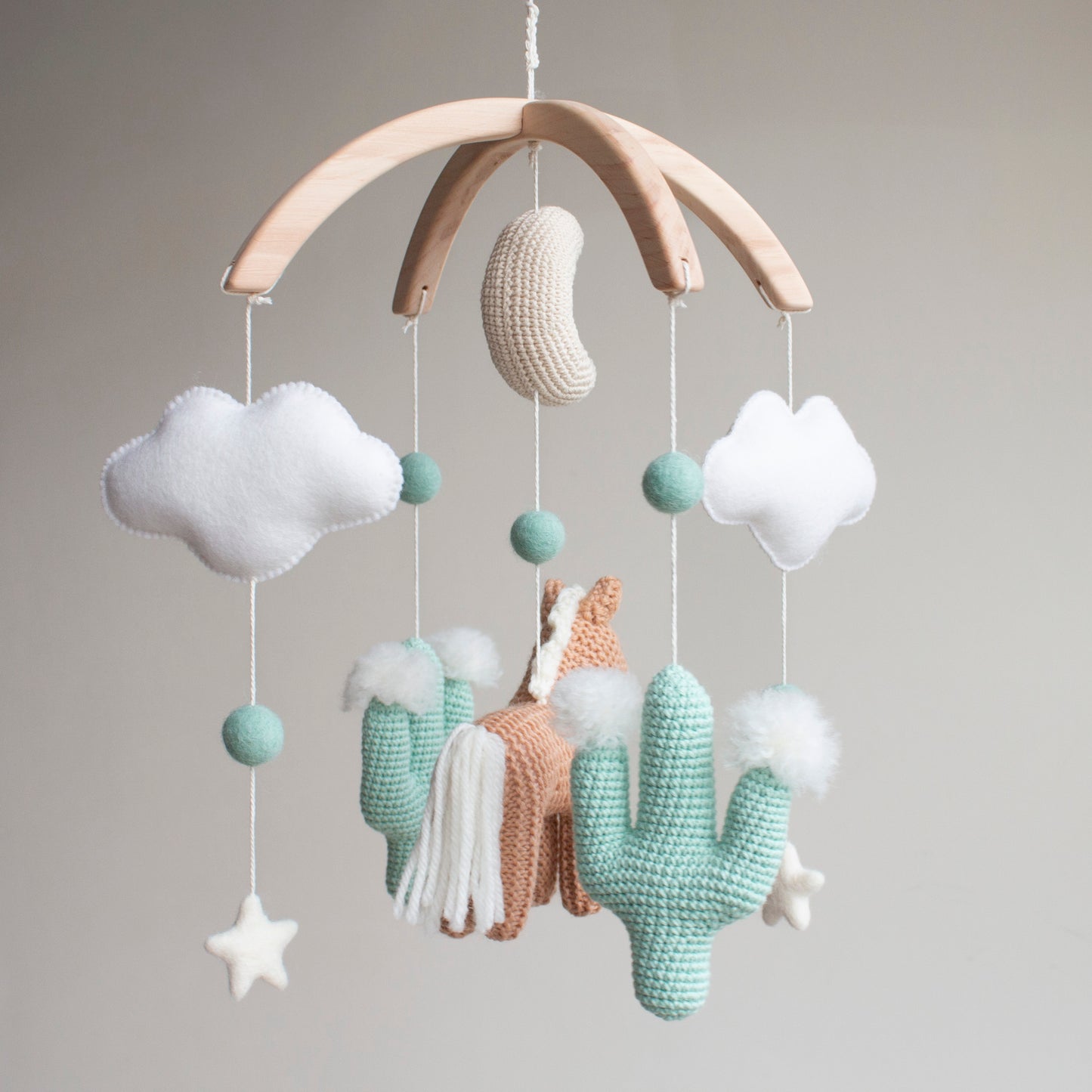 Handmade horse and cactus baby mobile in a muted mint, tan, and soft white palette. Every element is meticulously crafted using traditional "Slow Craft" techniques to ensure premium quality and durability. This nature-inspired accessory is a photogenic statement piece for a minimalist nursery, offering material transparency and safety for the baby's space. An ideal addition to UK baby registries, providing a high-end alternative to mass-market solutions for the discerning family