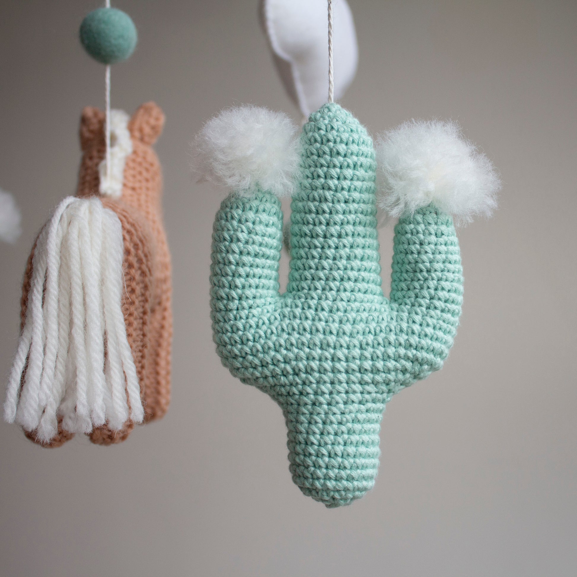 Detailed macro shot of a hand-crocheted mint green cactus with soft white wool pom-pom details, part of the Western horse mobile collection. Showcase of niche product specialization and artisan texture, our mobiles use only certified safe, non-toxic yarns. This close-up highlights the "Atelier" quality and material integrity that justifies a premium price point for affluent gift-vetted customers seeking heritage nursery art and unique, handcrafted keepsakes from Northern Ireland.