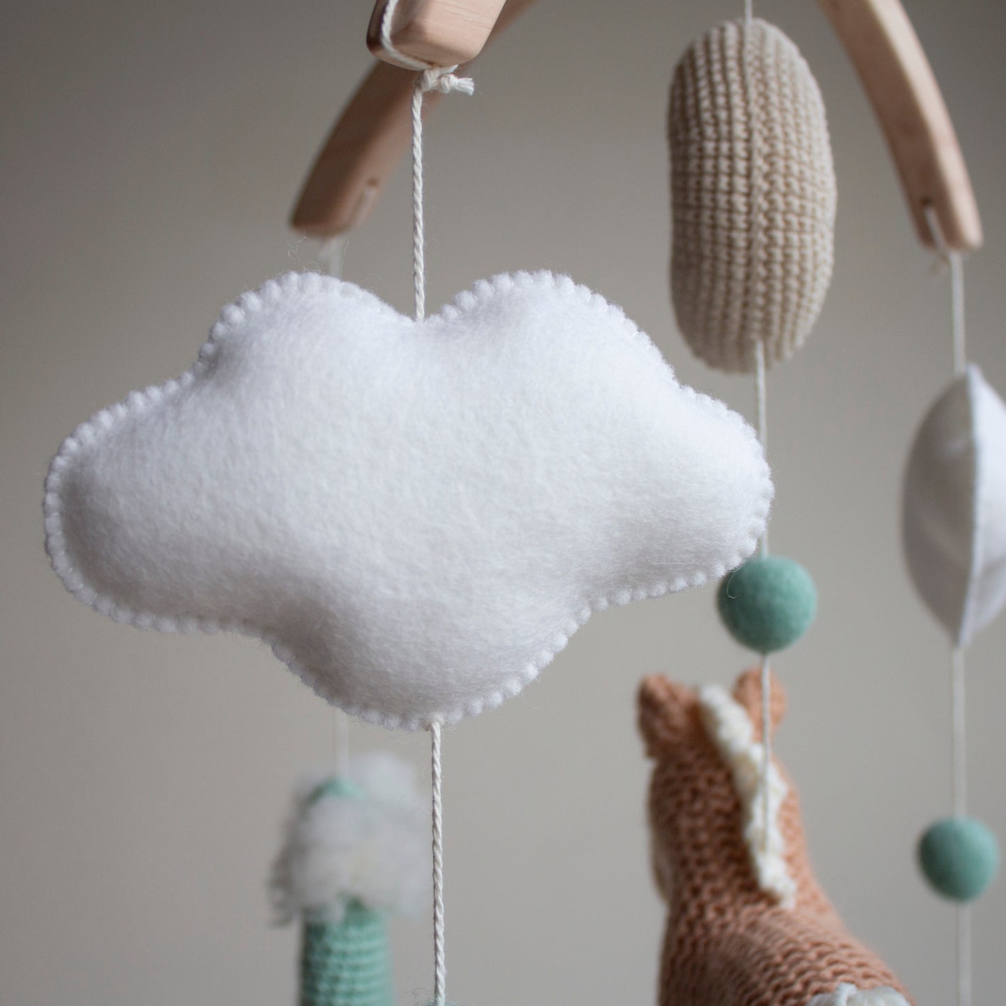 Close-up of a soft wool felt cloud and mint green accent ball on a Western-themed nursery mobile. Each cloud is carefully stitched for an airy and minimalist look, reflecting our commitment to design aesthetics and high-quality craftsmanship. These natural, sustainable elements create a tranquil sensory environment for a newborn, serving as a vetted heirloom gift that demonstrates a belief in ethical sourcing and support for small, independent UK artisan businesses.