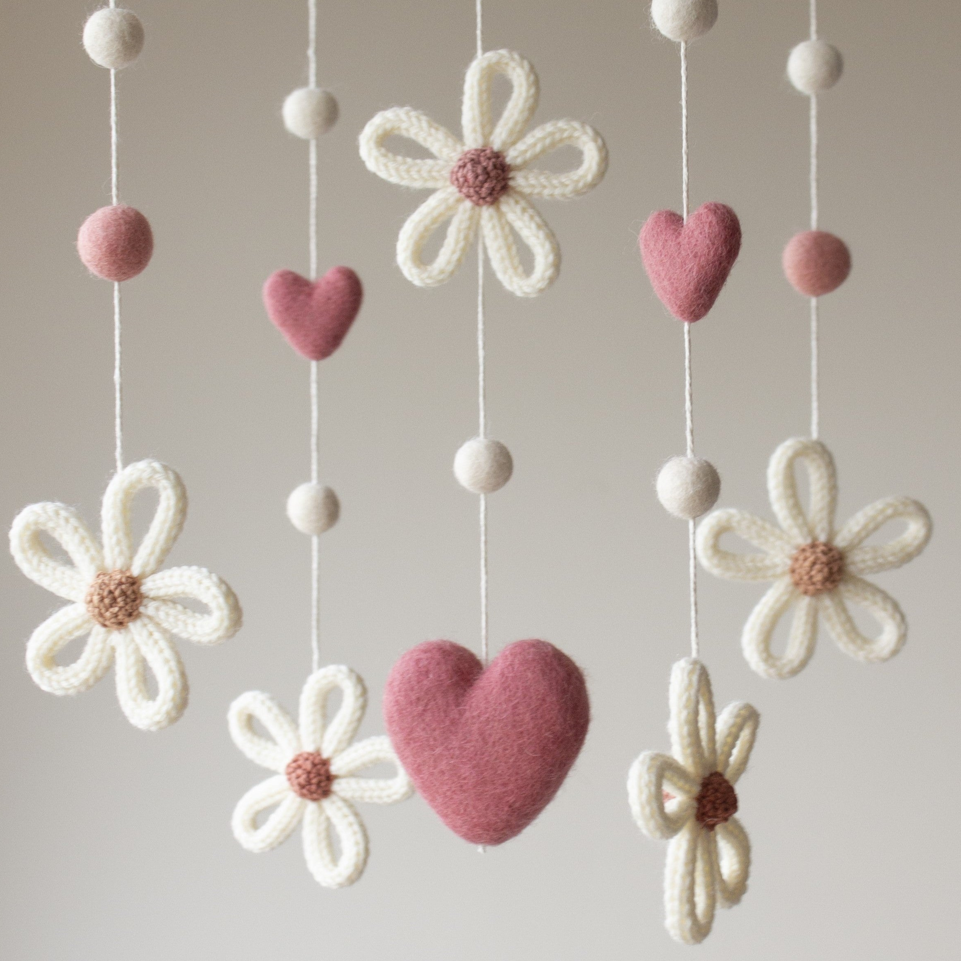Close up knitted daisies in soft creamy white with contrast centres in shades of tan, brick, dusty rose with dark pink hearts for baby visual stimulation.