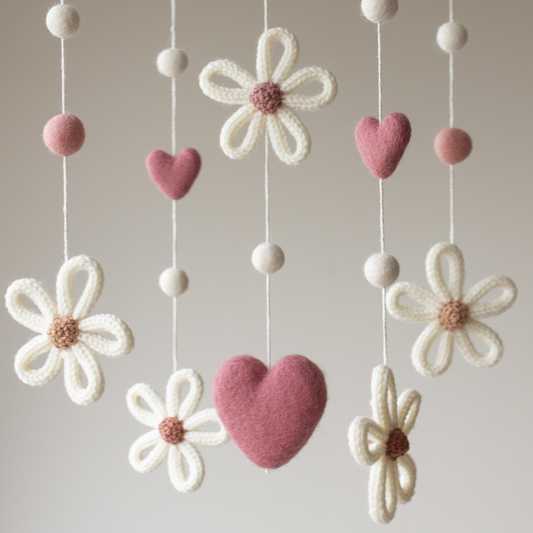 Close up knitted daisies in soft creamy white with contrast centres in shades of tan, brick, dusty rose with dark pink hearts for baby visual stimulation.